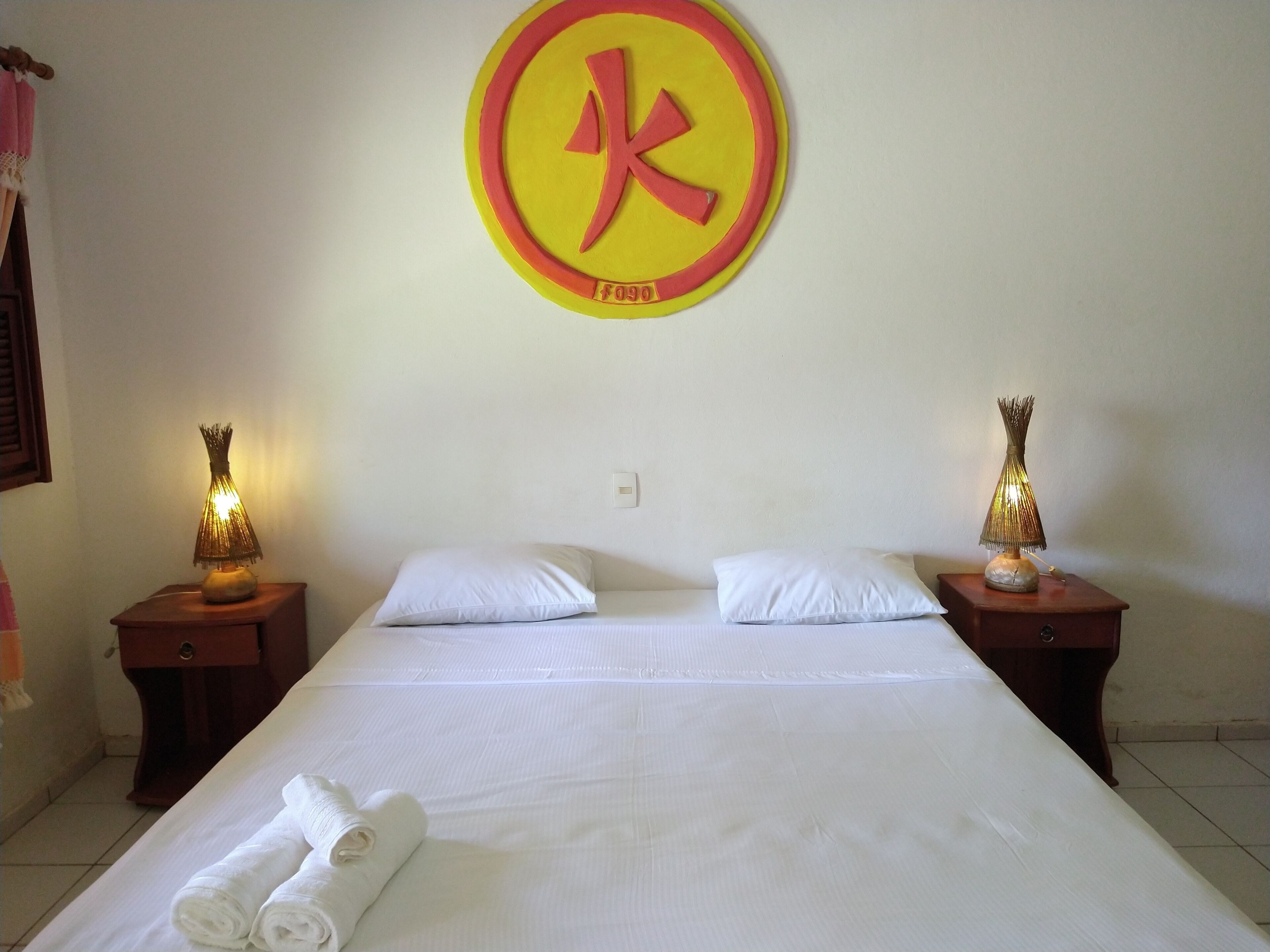 A hotel room with a bed, two bedside tables with lamps, a wall clock, and a towel on the bed.