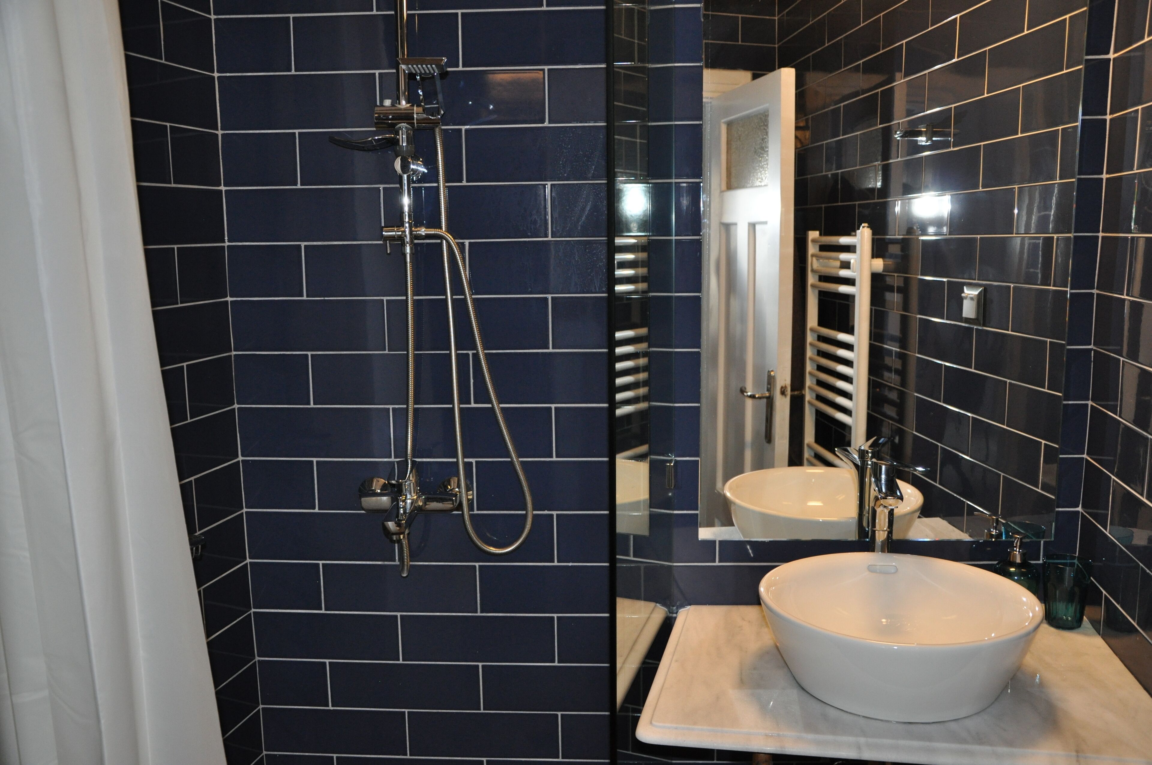 A bathroom with dark blue tiles, a white sink, and a shower with a handheld showerhead.