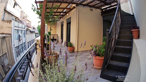 Un espacio exterior techado con una escalera, plantas en macetas y una barandilla de metal.