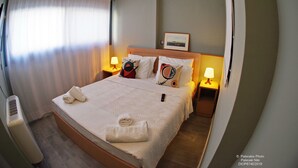 Una cama bien hecha con almohadas y una manta, una mesita de noche con una lámpara, y un cuadro en la pared.