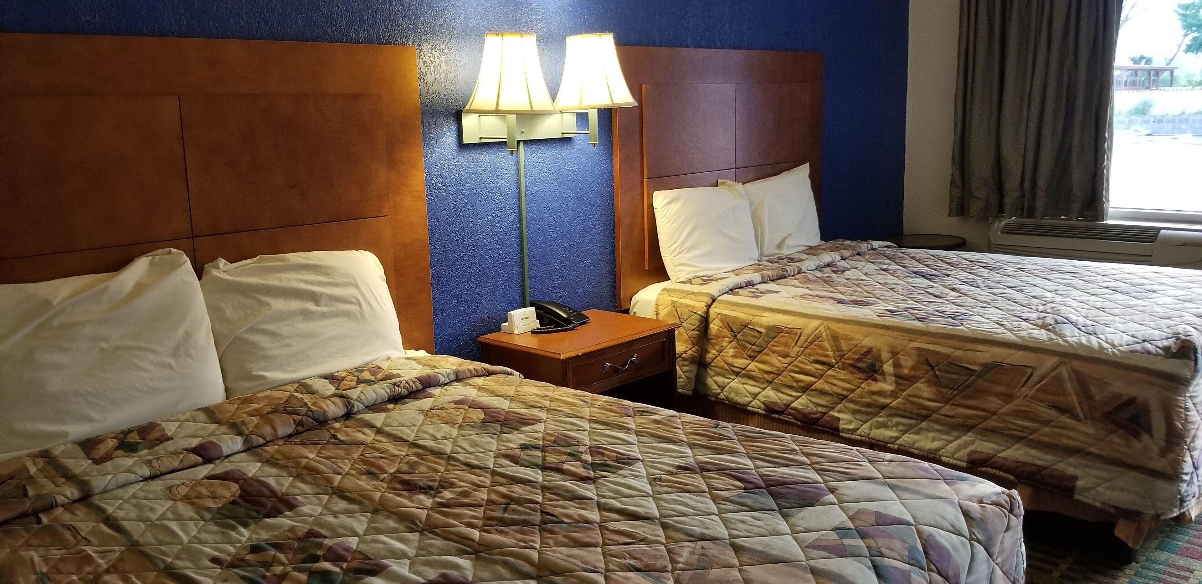 A hotel room with two beds, a nightstand with a lamp, and a window with curtains.