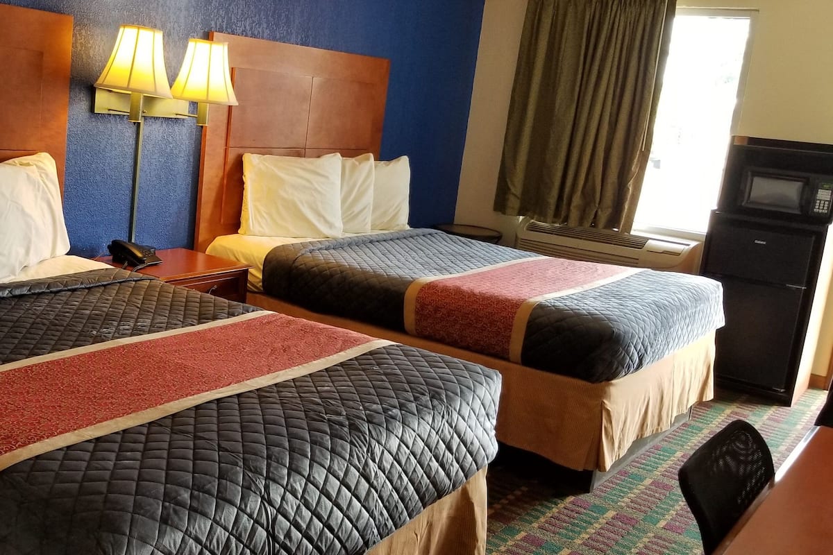 A hotel room with two beds, a desk, a lamp, a phone, and a microwave.