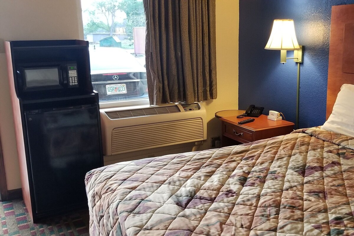 Ein Hotelzimmer mit Bett, Schreibtisch, Telefon, Lampe und Blick ins Freie.