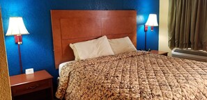 A hotel room with a wooden headboard, two bedside lamps, a bed with a patterned bedspread, a nightstand, and a thermostat. - Executive Inn (Victoria)