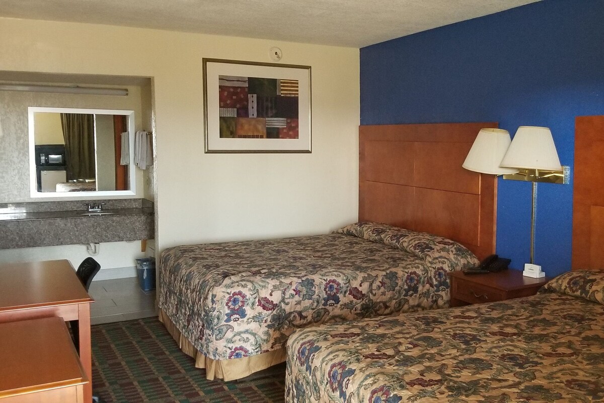 Habitación de hotel con dos camas, un escritorio, una silla, baño y un cuadro en la pared.