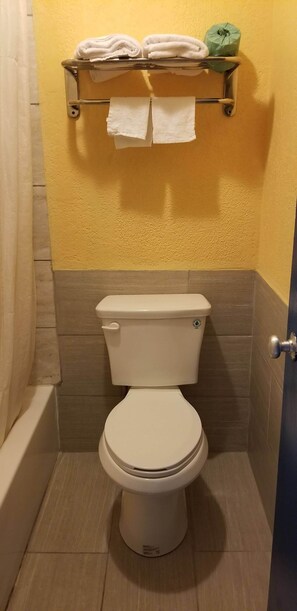 A bathroom with a toilet, a towel rack with towels, and a green bottle on the wall. - Executive Inn (Victoria)