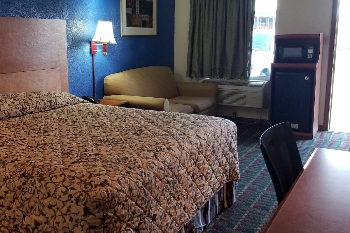 A hotel room with a large bed, a desk, a chair, a lamp, and a microwave.