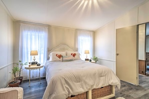 Un dormitorio con una cama, dos mesitas de noche con lámparas, una mesita auxiliar y dos plantas en macetas.