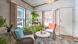 A sunroom with wicker furniture, a small table, and various potted plants. - Woodland Retreat: Near Trails, Golf & Wineries! (Harbor Springs)
