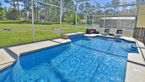 Una piscina con area coperta, un solarium con sedie e vista su una zona erbosa con alberi.