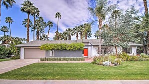A modern house with a red door, surrounded by a well-maintained lawn and tall palm trees.