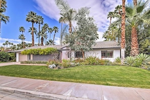 A modern house with a well-maintained lawn, palm trees, and a tiled roof.