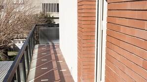 A narrow outdoor corridor with a metal railing, a brick wall, and a white building in the background. - M030 - Marcelli, new two-room apartment facing the sea (Marcelli)