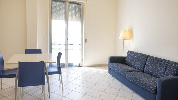 A room with a dining table, two chairs, a sofa, a lamp, and a sliding glass door. - M030 - Marcelli, new two-room apartment facing the sea (Marcelli)