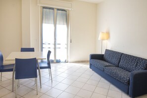 A room with a dining table, two chairs, a sofa, a lamp, and a sliding glass door. - M030 - Marcelli, new two-room apartment facing the sea (Marcelli)