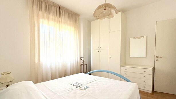 Una camera da letto con un letto, un armadio, una cassettiera, uno specchio e una finestra con tende.