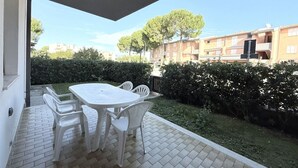 Una terrazza esterna con tavolo e sedie, pavimento piastrellato e vista su edifici residenziali e alberi.