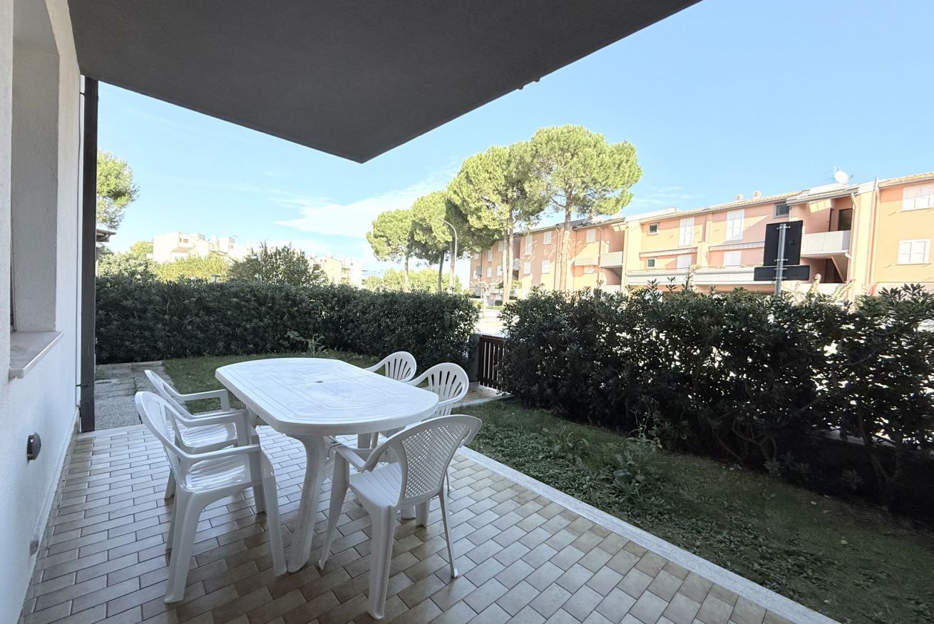 Um pátio externo com mesa e cadeiras, piso ladrilhado e vista para edifícios residenciais e árvores.