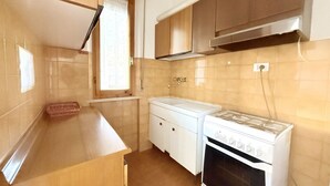 Una cucina con mobili in legno, un fornello bianco e una finestra con tenda.