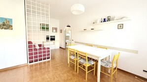 Un'area pranzo con tavolo e sedie bianche, un divisorio bianco e una lampada a sospensione.