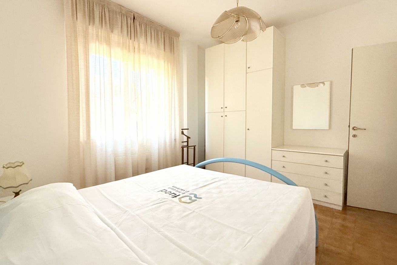 Une chambre à coucher comprenant un lit, une armoire, une commode, un miroir et une fenêtre avec des rideaux.