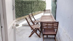 Un patio con un tavolo e sedie di legno, una porta bianca e un siepe sullo sfondo.