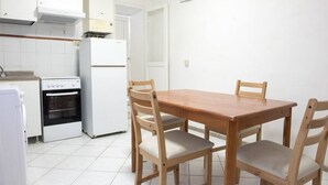 Cucina con mobili bianchi, piano cottura, forno e frigorifero. È presente un tavolo da pranzo in legno con quattro sedie.