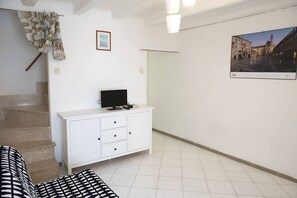 A room with a staircase, a white cabinet with a television, a patterned sofa, and a framed picture on the wall.
