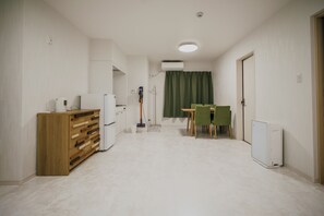 Eine kleine Küche mit einem Holzkorpus, einem weißen Kühlschrank und einer Essecke mit grünem Tisch und Stühlen.