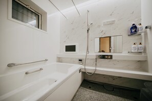 Ein modernes Badezimmer mit einer weißen Badewanne, einer Handbrause, einem eingebauten Spiegel und einem Ablagefach mit Pflegeprodukten.