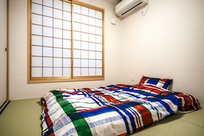 A room with tatami flooring, a shoji screen window, and a bed with a colorful quilt.