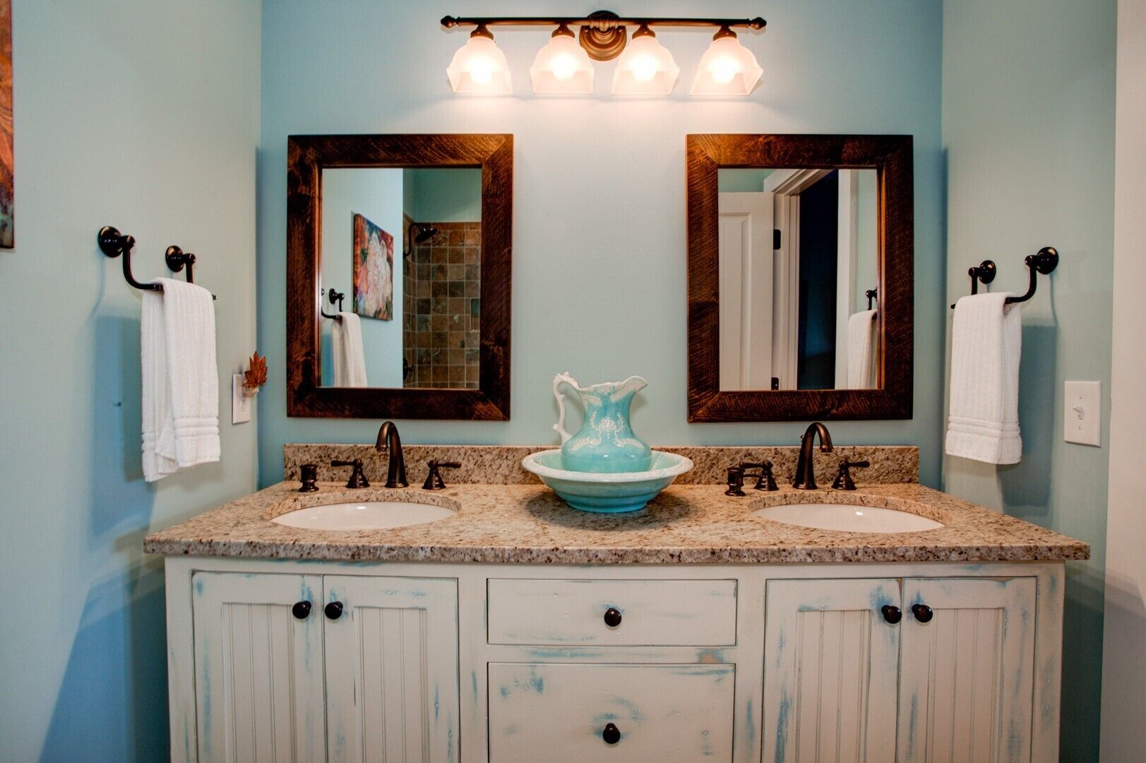 A bathroom with two sinks, a large mirror, and a decorative pitcher.