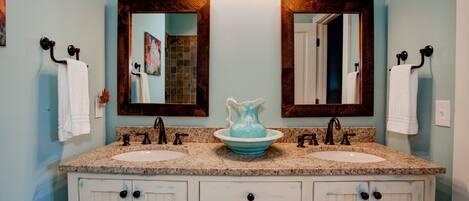 A bathroom with two sinks, a large mirror, and a decorative pitcher.