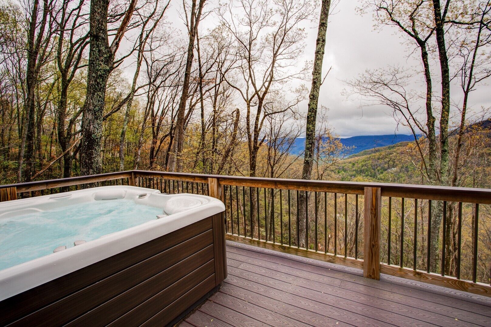 A hot tub on a wooden deck with a view of a forest and mountains.