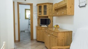 A wooden cabinet with a television, a bowl of fruit, and a white chair in a room with tiled flooring and a door leading to another room. - M255 - Marcelli, three-room apartment with porch 250m from the sea (Marcelli)