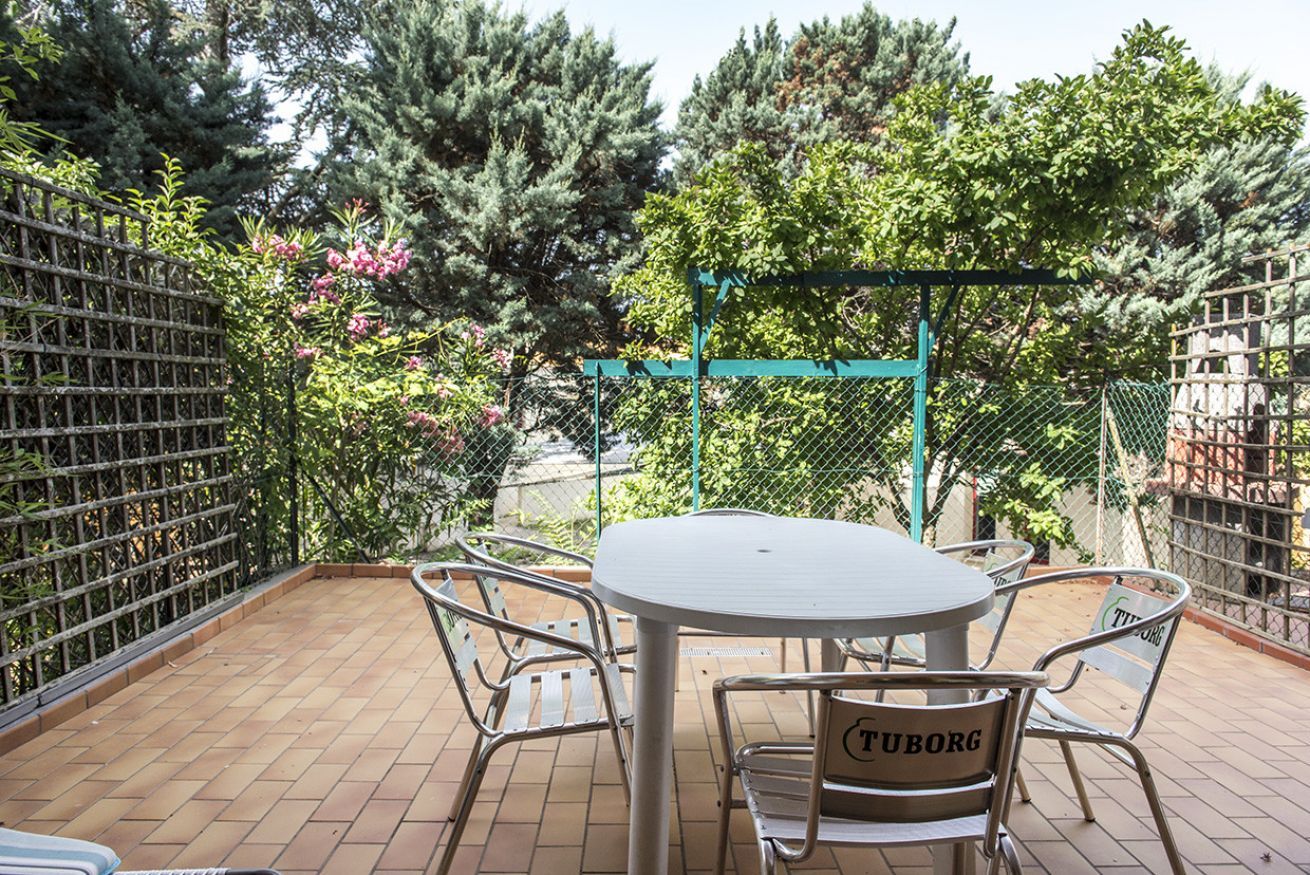Une terrasse avec une table ronde et des chaises, entourée d’une clôture en métal et d’arbres.