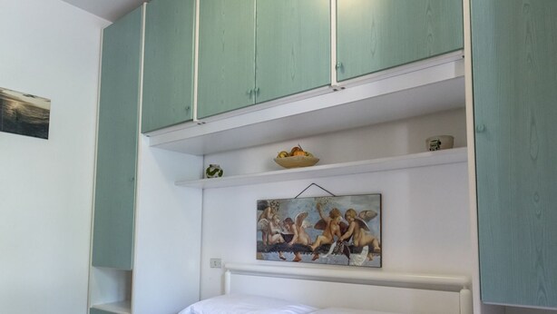 A bedroom with a bed, a green cabinet above, a shelf with a fruit bowl and a painting. - M255 - Marcelli, three-room apartment with porch 250m from the sea (Marcelli)
