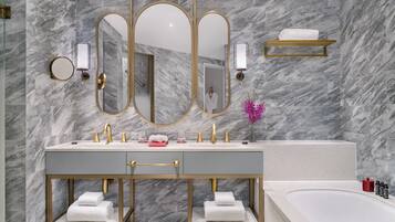 A modern bathroom with a marble wall, a double sink with gold fixtures, a large mirror, and a bathtub.