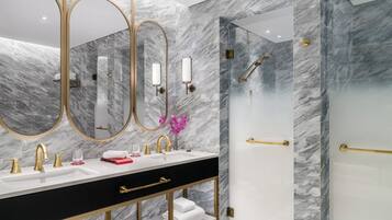 A modern bathroom with a marble wall, a black vanity with gold fixtures, a large mirror, and a glass-enclosed shower.