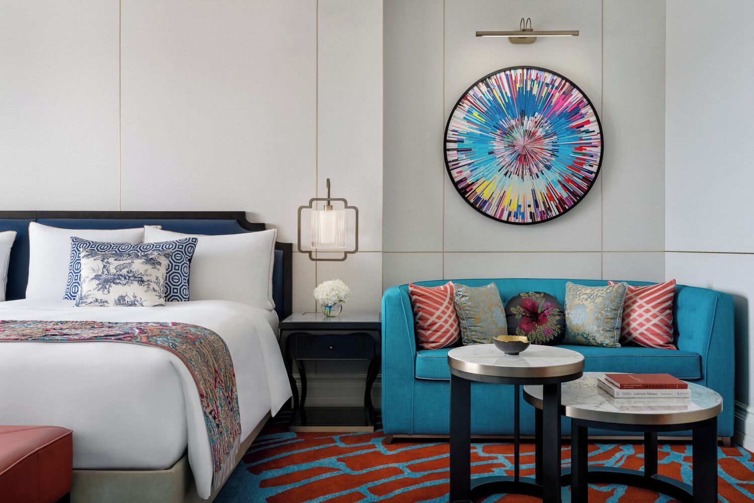 Una habitación de hotel con una cama, un sofá azul, una mesita y una obra de arte colorida en la pared.