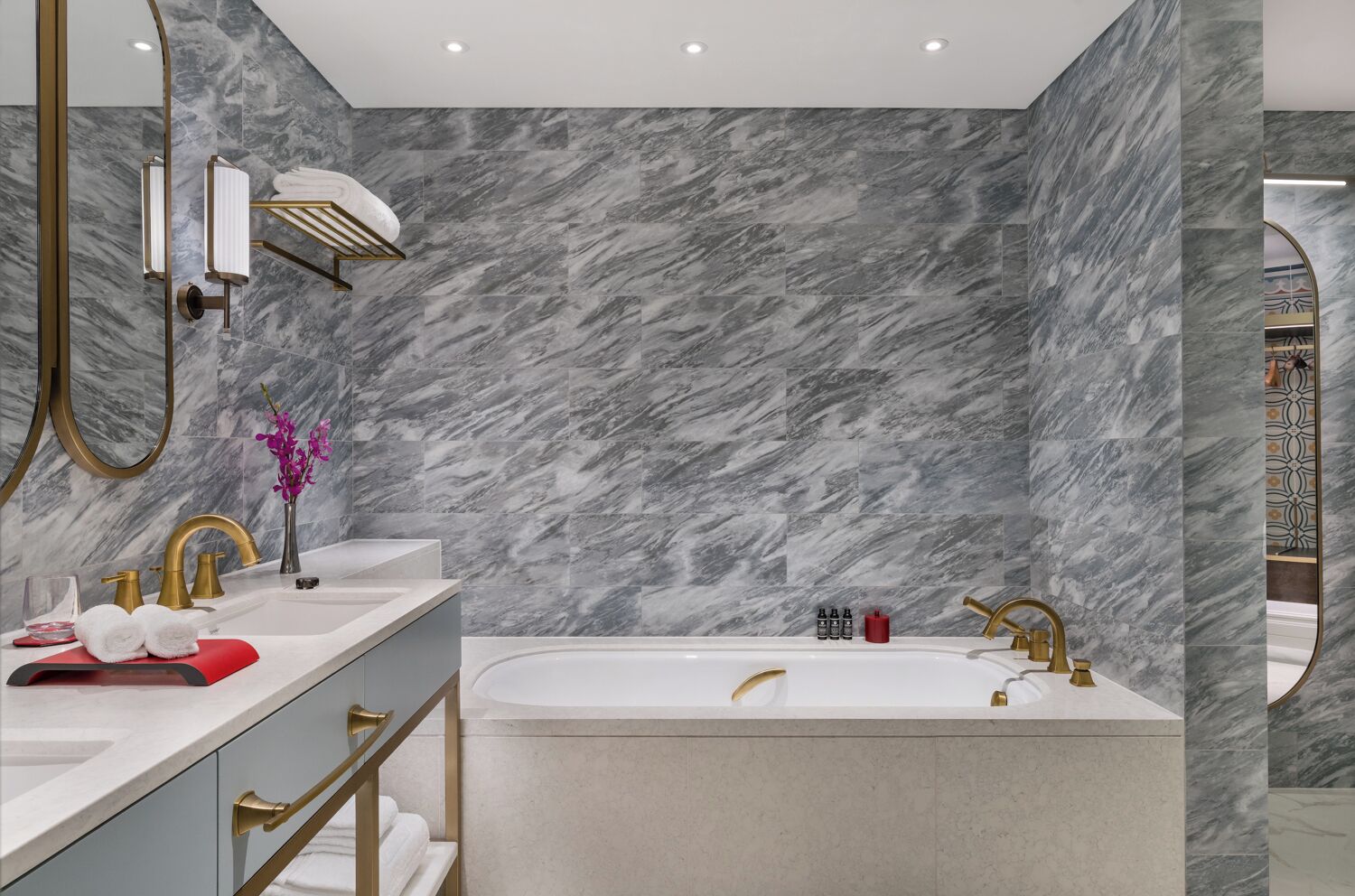 Une salle de bain moderne avec un mur en marbre, une baignoire sur pieds et des accessoires dorés.