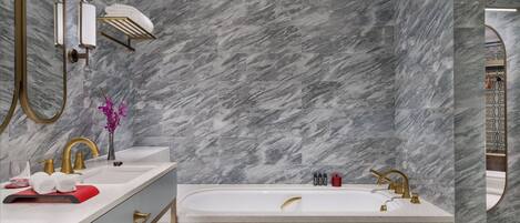 Une salle de bain moderne avec un mur en marbre, une baignoire sur pieds et des accessoires dorés.