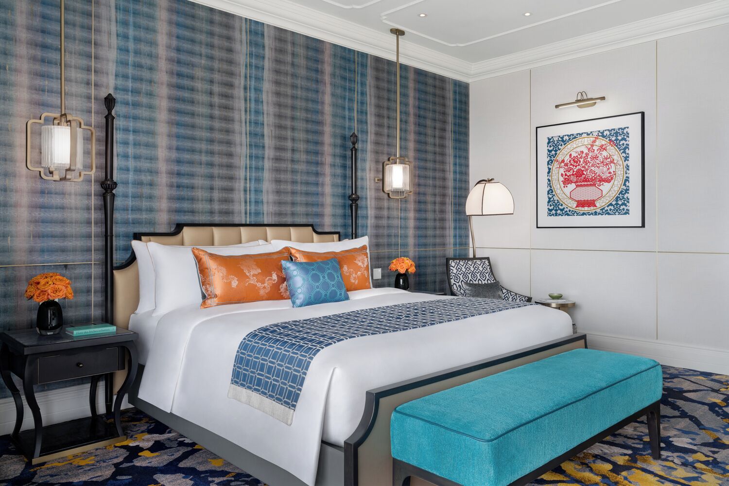 Una habitación de hotel moderna con una cama grande, un banco, una mesita de noche, una lámpara y una obra de arte enmarcada en la pared.