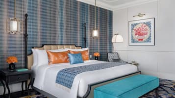 Una habitación de hotel moderna con una cama grande, un banco, una mesita de noche, una lámpara y una obra de arte enmarcada en la pared.