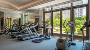 A spacious gym with treadmills, ellipticals, and a rowing machine, large windows offering views of a cityscape and greenery. - Grand Lisboa Palace Macau (Cotai)