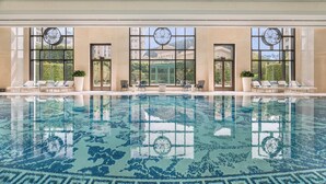 A large indoor swimming pool with clear blue water, surrounded by lounge chairs and large windows with decorative glass patterns. - Grand Lisboa Palace Macau (Cotai)