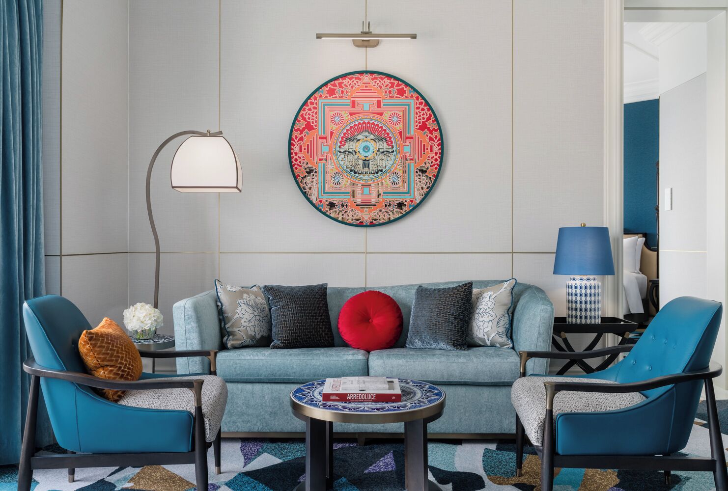 Een moderne woonkamer met een blauwgroene bank, twee blauwe fauteuils, een ronde salontafel en een decoratieve wandversiering.