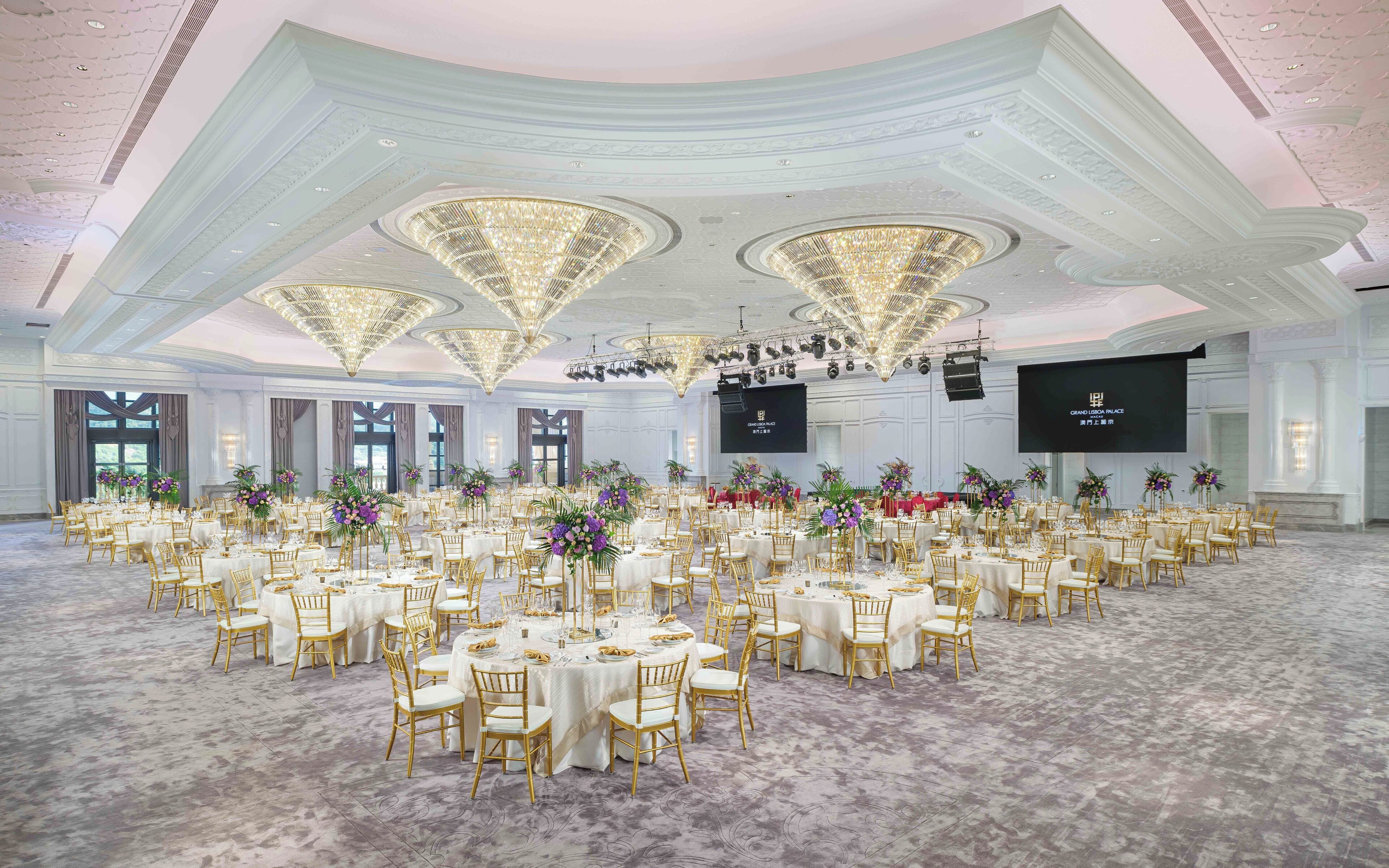 A large banquet hall with round tables, gold chairs, and floral centerpieces.