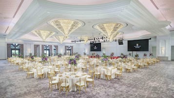 A large banquet hall with round tables, gold chairs, and floral centerpieces.