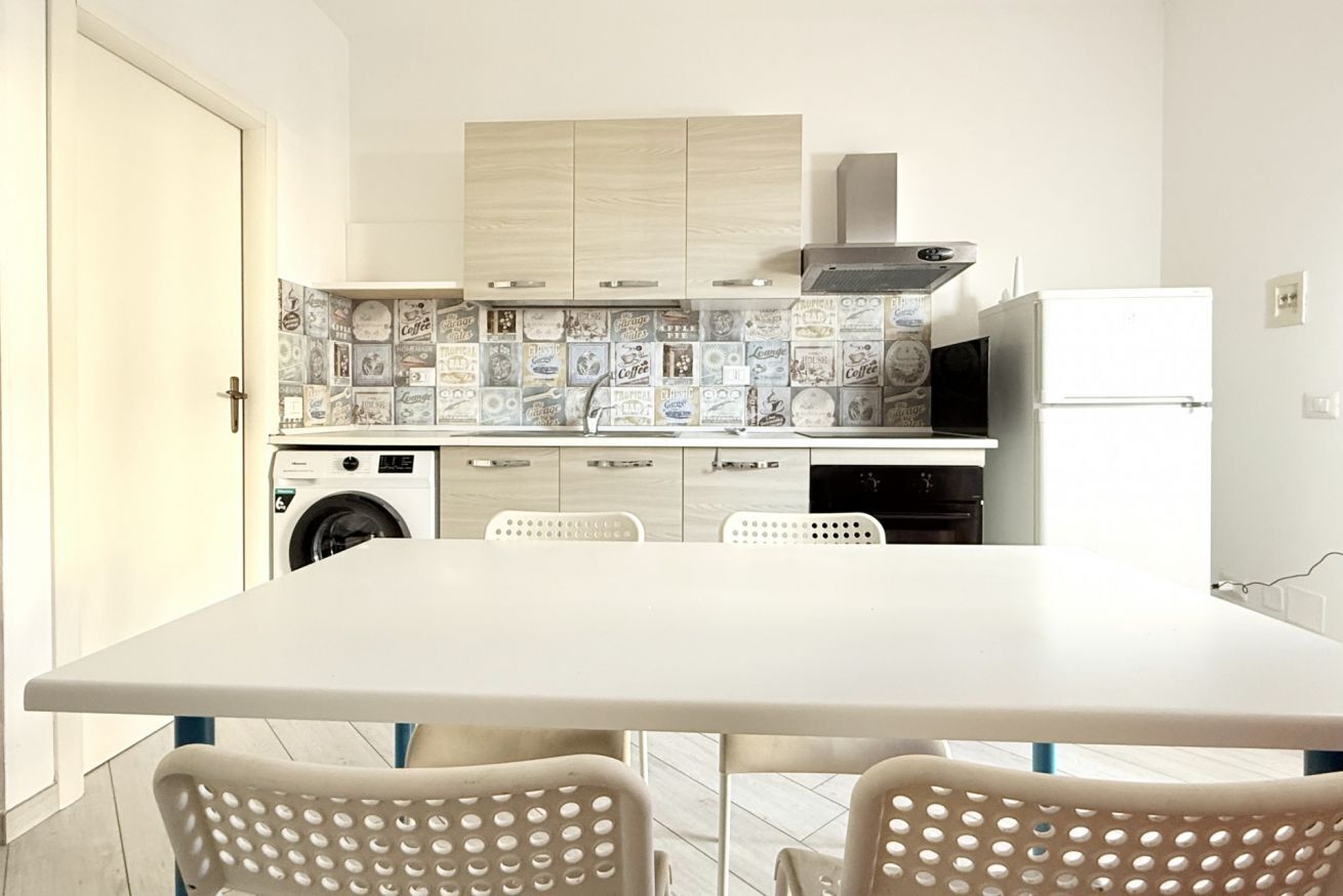 Une cuisine compacte équipée d’un lave-linge, d’un four à micro-ondes et d’un réfrigérateur. On y trouve également une table à manger avec des chaises.